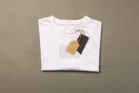 Téléchargez les photos : T-shirt plié blanc avec étiquettes avec espace de copie sur fond marron. Mode, vêtements, concept de couleur et de tissu. - en image libre de droit