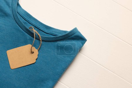 Téléchargez les photos : Gros plan de la couche plate de t-shirt bleu avec étiquette et espace de copie sur fond de tableaux blancs. Mode, vêtements, concept de couleur et de tissu. - en image libre de droit