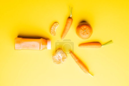 Téléchargez les photos : Gros plan de la bouteille avec jus, carottes et mandarines avec espace de copie sur fond jaune. Fruits, nourriture, fraîcheur et concept de couleur. - en image libre de droit