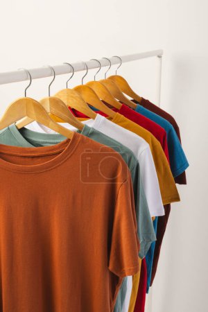 Multi coloured t shirts on hangers hanging from clothes rail and copy space on white background. Fashion, clothes, colour and fabric concept.