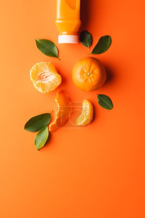 Foto de Primer plano de la botella con jugo, mandarina, segmentos y hojas con espacio de copia sobre fondo naranja. Concepto de frutas, alimentos, frescura y color. - Imagen libre de derechos