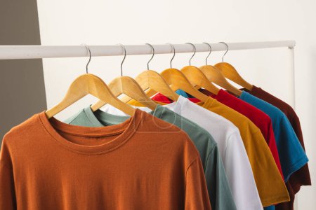 Bunte T-Shirts auf Kleiderbügeln hängen an der Kleiderstange und kopieren Platz auf weißem Hintergrund. Mode, Kleidung, Farb- und Stoffkonzept.