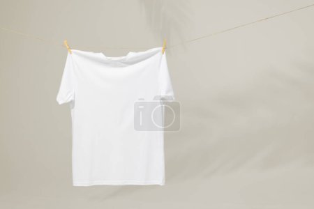 Foto de Camiseta blanca colgando de la línea de ropa con clavijas y espacio de copia sobre fondo gris. Moda, ropa, color y concepto de tela. - Imagen libre de derechos