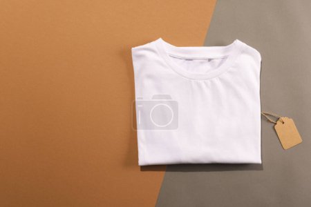 Foto de Primer plano de la camiseta blanca doblada con etiqueta y espacio de copia sobre fondo marrón. Moda, ropa, color y concepto de tela. - Imagen libre de derechos