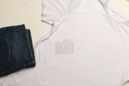 Téléchargez les photos : Gros plan de la couche plate de t-shirt blanc, pantalon en denim et espace de copie sur fond de tableaux blancs. Mode, vêtements, concept de couleur et de tissu. - en image libre de droit