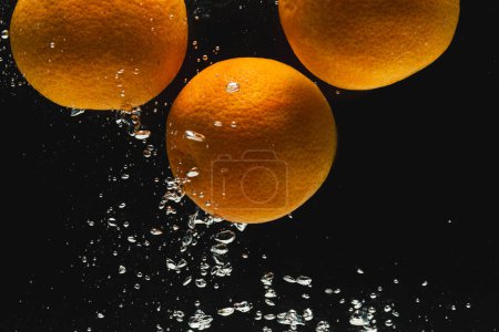 Téléchargez les photos : Gros plan d'oranges tombant dans l'eau avec espace de copie sur fond noir. Fruits, nourriture, fraîcheur et concept de couleur. - en image libre de droit