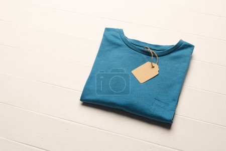 Photo for Close up of flat lay of blue t shirt with tag and copy space on white boards background. Fashion, clothes, colour and fabric concept. - Royalty Free Image