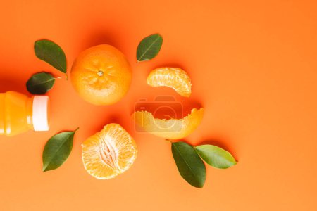 Foto de Primer plano de la botella con jugo, mandarina, segmentos y hojas con espacio de copia sobre fondo naranja. Concepto de frutas, alimentos, frescura y color. - Imagen libre de derechos