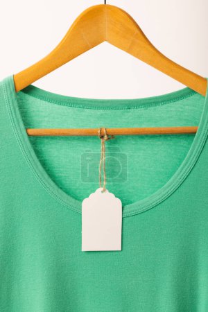 Téléchargez les photos : T-shirt vert avec étiquette sur cintre avec espace de copie sur fond blanc. Mode, vêtements, concept de couleur et de tissu. - en image libre de droit