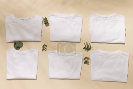 Téléchargez les photos : Gros plan de t-shirts pliés blancs avec des feuilles et de l'espace de copie sur fond jaune. Mode, vêtements, concept de couleur et de tissu. - en image libre de droit