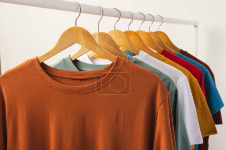 Foto de Camisetas multicolores en perchas colgadas de riel de ropa y espacio de copia sobre fondo blanco. Moda, ropa, color y concepto de tela. - Imagen libre de derechos