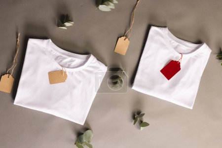Photo for Folded white t shirts with tags and leaves with copy space on brown background. Fashion, clothes, colour and fabric concept. - Royalty Free Image