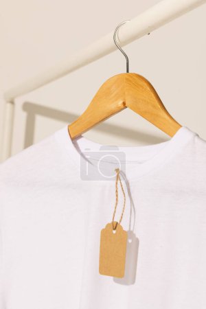 Foto de Camiseta blanca con etiqueta colgando de perchero con espacio de copia sobre fondo blanco. Moda, ropa, color y concepto de tela. - Imagen libre de derechos