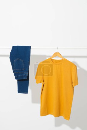 Téléchargez les photos : T-shirt jaune et pantalon en denim sur rail de vêtements avec espace de copie sur fond blanc. Mode, vêtements, concept de couleur et de tissu. - en image libre de droit