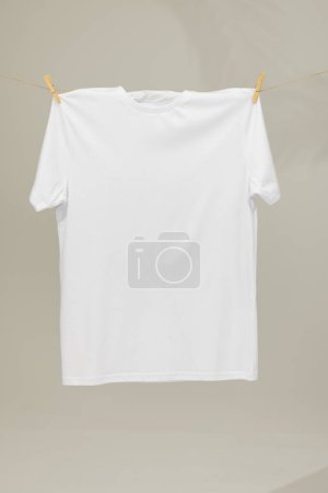 Foto de Camiseta blanca colgando de la línea de ropa con clavijas y espacio de copia sobre fondo gris. Moda, ropa, color y concepto de tela. - Imagen libre de derechos