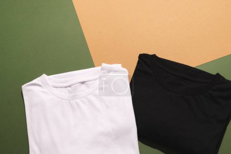 Téléchargez les photos : Gros plan des t-shirts pliés blancs et noirs et de l'espace de copie sur fond vert à orange. Mode, vêtements, concept de couleur et de tissu. - en image libre de droit