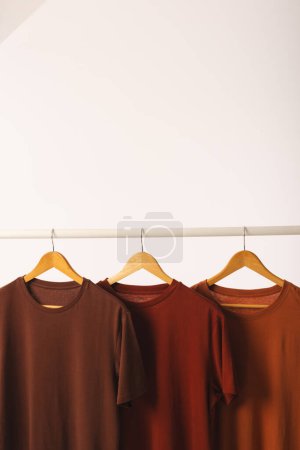 Foto de Tres camisetas marrones en perchas colgando de riel de ropa y espacio de copia sobre fondo blanco. Moda, ropa, color y concepto de tela. - Imagen libre de derechos