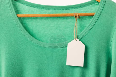 Téléchargez les photos : T-shirt vert avec étiquette sur cintre avec espace de copie sur fond blanc. Mode, vêtements, concept de couleur et de tissu. - en image libre de droit