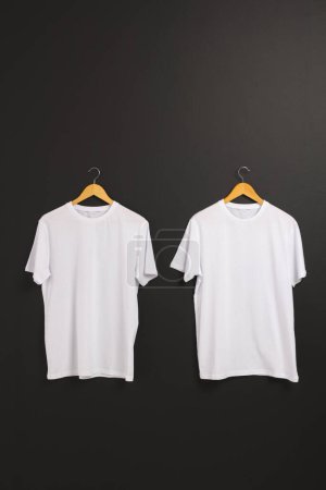 Téléchargez les photos : Deux t-shirts blancs sur cintres et copier l'espace sur fond noir. Mode, vêtements, concept de couleur et de tissu. - en image libre de droit