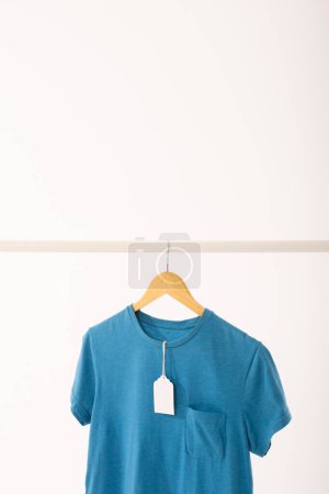Photo for Blue t shirt with tag on hanger hanging from clothes rail with copy space on white background. Fashion, clothes, colour and fabric concept. - Royalty Free Image