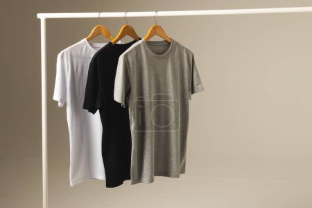 Téléchargez les photos : Trois t-shirts sur cintres suspendus à des vêtements rail et copier l'espace sur fond gris. Mode, vêtements, concept de couleur et de tissu. - en image libre de droit