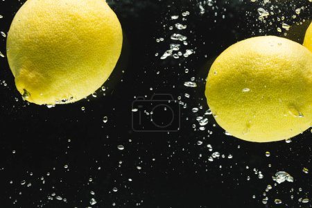 Photo for Close up of lemons falling into water with copy space on black background. Fruit, food, freshness and colour concept. - Royalty Free Image