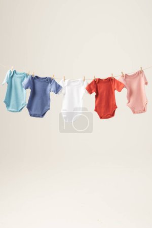 Téléchargez les photos : Bébé multicolore pousse suspendu à la ligne de vêtements avec des chevilles et de l'espace de copie sur fond blanc. Mode bébé, vêtements, concept de couleur et de tissu. - en image libre de droit