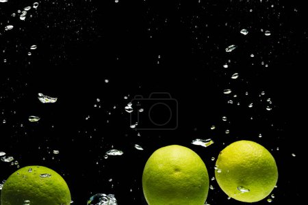 Téléchargez les photos : Gros plan de limes tombant dans l'eau avec espace de copie sur fond noir. Fruits, nourriture, fraîcheur et concept de couleur. - en image libre de droit