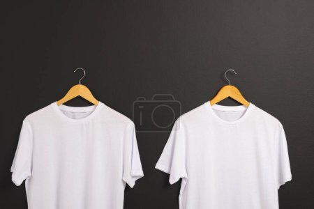 Téléchargez les photos : Deux t-shirts blancs sur cintres et copier l'espace sur fond noir. Mode, vêtements, concept de couleur et de tissu. - en image libre de droit