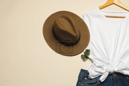 Téléchargez les photos : Pose plate de t-shirt blanc, chapeau de soleil et jupe en denim avec espace de copie sur fond crème. Mode, vêtements, concept de couleur et de tissu. - en image libre de droit