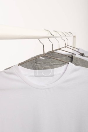 Foto de Camisetas blancas y grises en perchas colgadas de riel de ropa y espacio de copia sobre fondo blanco. Moda, ropa, color y concepto de tela. - Imagen libre de derechos