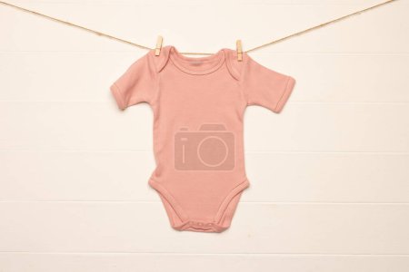 Foto de Bebé rosa crecer colgando con clavijas de ropa con espacio de copia sobre fondo blanco. Moda de bebé, ropa, color y concepto de tela. - Imagen libre de derechos