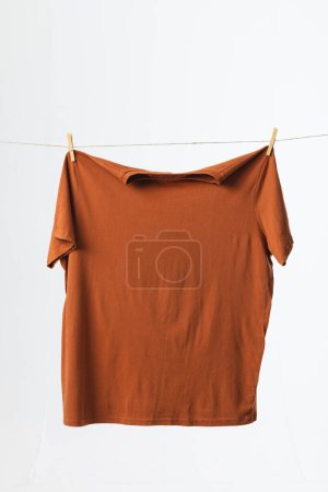 Foto de Camiseta marrón colgando de la línea de ropa con clavijas y espacio de copia sobre fondo blanco. Moda, ropa, color y concepto de tela. - Imagen libre de derechos