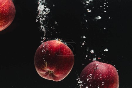 Foto de Primer plano de manzanas rojas que caen al agua con espacio de copia sobre fondo negro. Concepto de frutas, alimentos, frescura y color. - Imagen libre de derechos