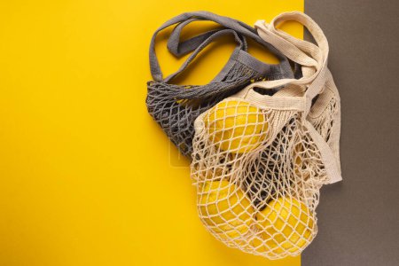 Photo for Brown and ecru mesh net bags with lemons and copy space on brown and yellow background. Shopping, bag, colour, fabric, texture and materials concept. - Royalty Free Image