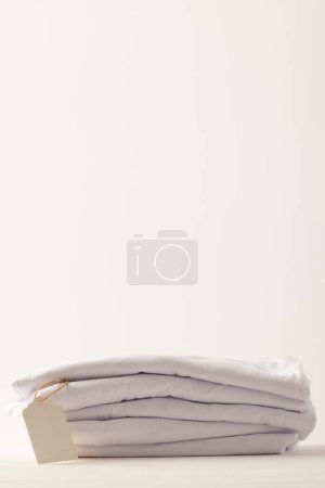 Téléchargez les photos : Empilement de t-shirts blancs avec étiquette et espace de copie sur fond blanc. Mode, vêtements, concept de couleur et de tissu. - en image libre de droit
