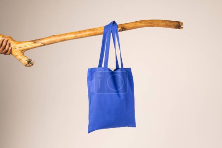 Photo for Blue canvas bag hanging from wooden branch with copy space on white background. Shopping, bag, colour, fabric, texture and materials concept. - Royalty Free Image