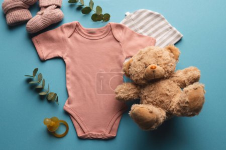 Photo for Flat lay of pink baby grow, hat, teddy bear and pink booties with copy space on blue background. Baby fashion, clothes, colour and fabric concept. - Royalty Free Image