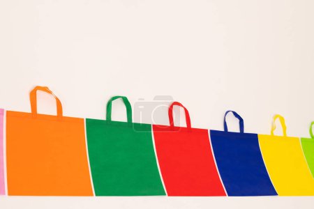 Téléchargez les photos : Rangée de sacs en toile multicolores avec espace de copie sur fond blanc. Shopping, sac, couleur, tissu, texture et matériaux concept. - en image libre de droit