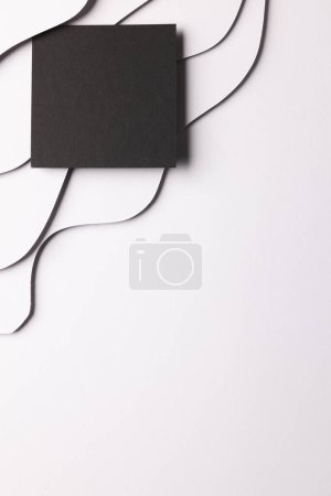 Foto de Imagen vertical del cuadrado de papel negro con espacio de copia sobre ondas blancas de papel sobre fondo blanco. Concepto de papel, escritura, textura y materiales. - Imagen libre de derechos