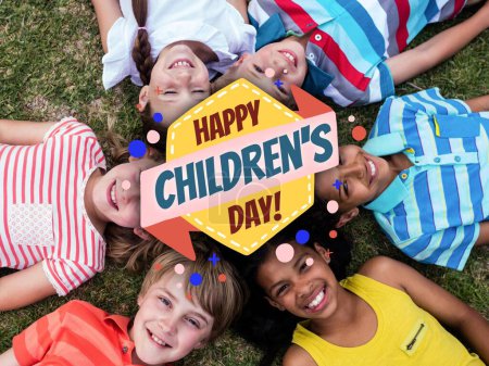 Foto de Composición de texto feliz día de los niños y diversos niños sonriendo acostados en la hierba. Día de los niños, concepto de infancia y felicidad imagen generada digitalmente. - Imagen libre de derechos