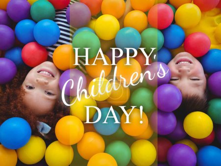 Foto de Composición de texto del día de los niños felices y niños biraciales sonriendo acostados en bolas de colores. Día de los niños, concepto de infancia y felicidad imagen generada digitalmente. - Imagen libre de derechos