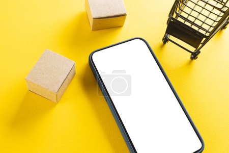 Photo for Smartphone with copy space and trolley with boxes on yellow background. Cyber monday, cyber shopping, retail, technology, electronic device and communication concept. - Royalty Free Image