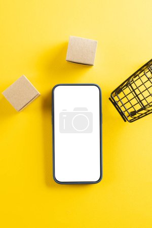 Photo for Vertical image of smartphone with copy space and trolley with boxes on yellow background. Cyber monday, cyber shopping, retail, technology, electronic device and communication concept. - Royalty Free Image