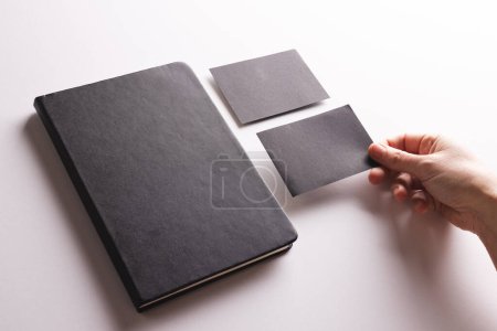 Foto de Cuaderno negro y mujer caucásica sosteniendo la tarjeta de papel negro sobre fondo blanco. Concepto de papel, escritura, textura y materiales. - Imagen libre de derechos