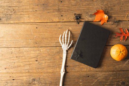 Photo for Halloween decorations and skeleton hand next to notebook with copy space on brown background. Fall, autumn, halloween, tradition and celebration concept. - Royalty Free Image