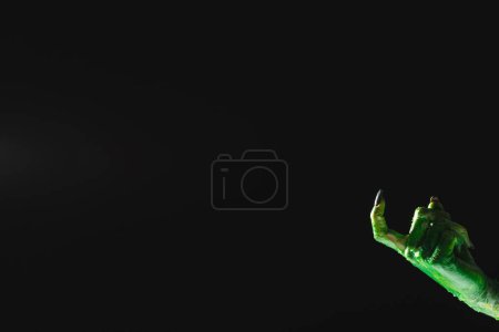 Foto de Mano monstruo verde con uñas negras apuntando con el dedo sobre fondo negro. Halloween, tradición y concepto de celebración. - Imagen libre de derechos