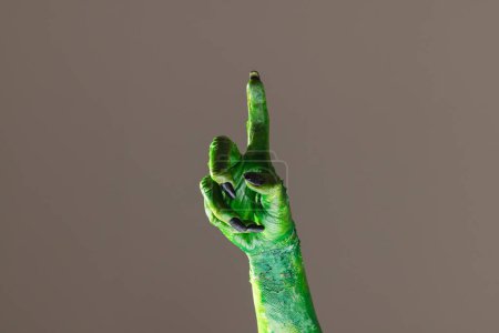 Téléchargez les photos : Main monstre vert avec des ongles noirs pointant avec le doigt sur fond gris. Halloween, concept de tradition et célébration. - en image libre de droit