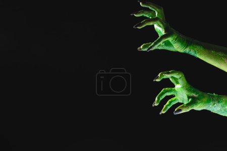 Téléchargez les photos : Mains de monstre vert avec des ongles noirs atteignant sur fond noir. Halloween, concept de tradition et célébration. - en image libre de droit