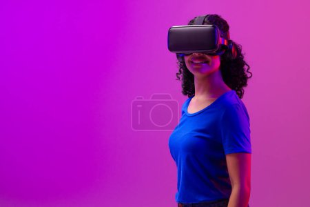 Téléchargez les photos : Femme Biracial utilisant vr casque sur fond rose fluo à violet. Technologie, réseaux numériques, connexions mondiales et métaverse de la communication. - en image libre de droit
